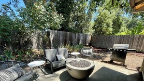 A backyard with a gray sofa, two chairs, a round table, a fire pit, and a grill. - Prime Location, Downtown Murphys (Murphys)