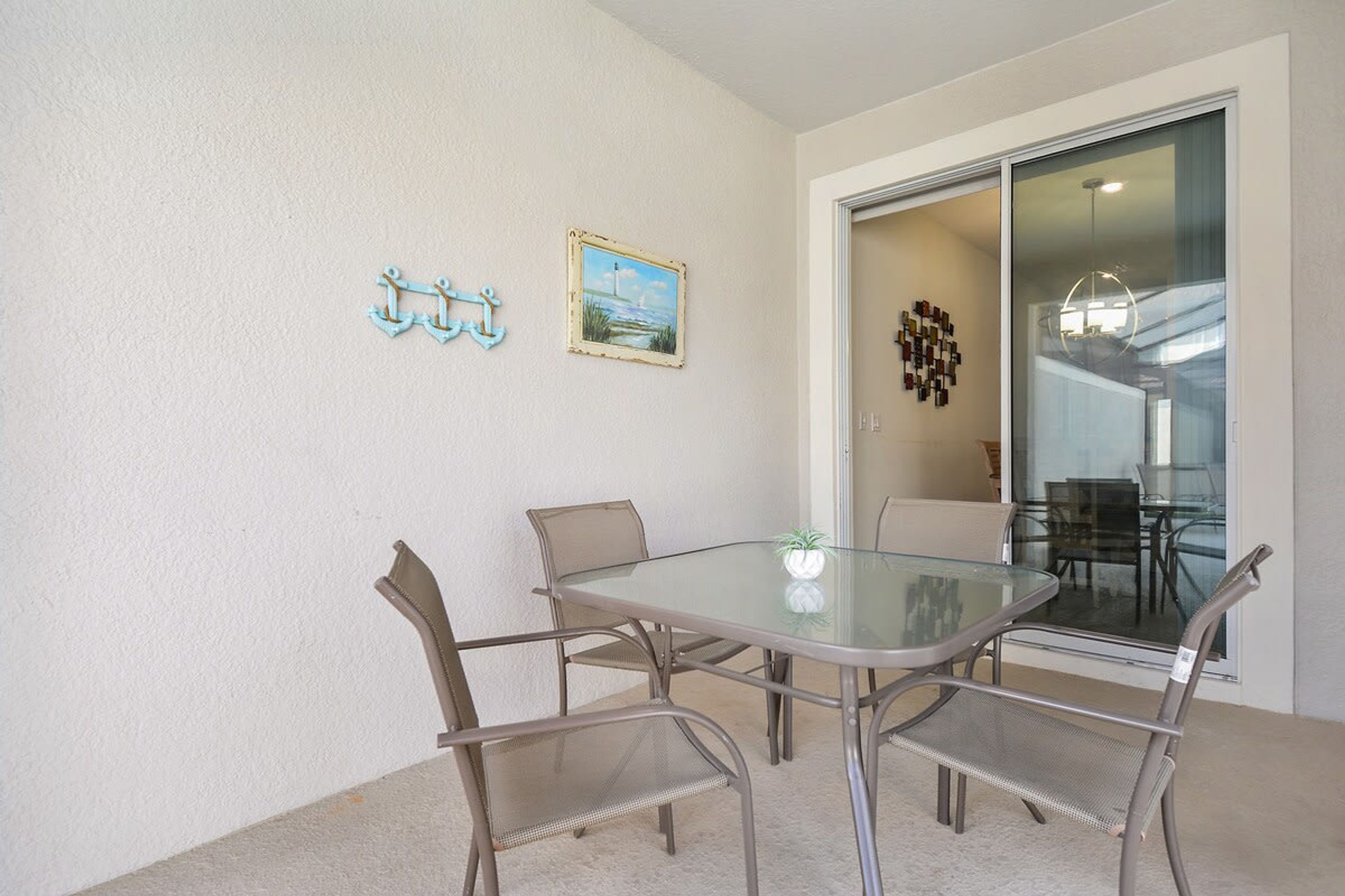 A dining area with a glass table and four chairs, a painting, and a decorative metal piece on the wall.