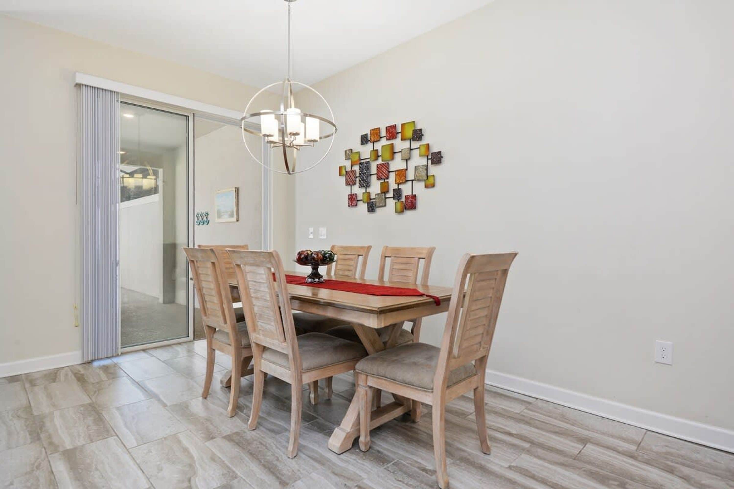 Un coin repas comprenant une table en bois, six chaises, un lustre et une œuvre d’art murale.