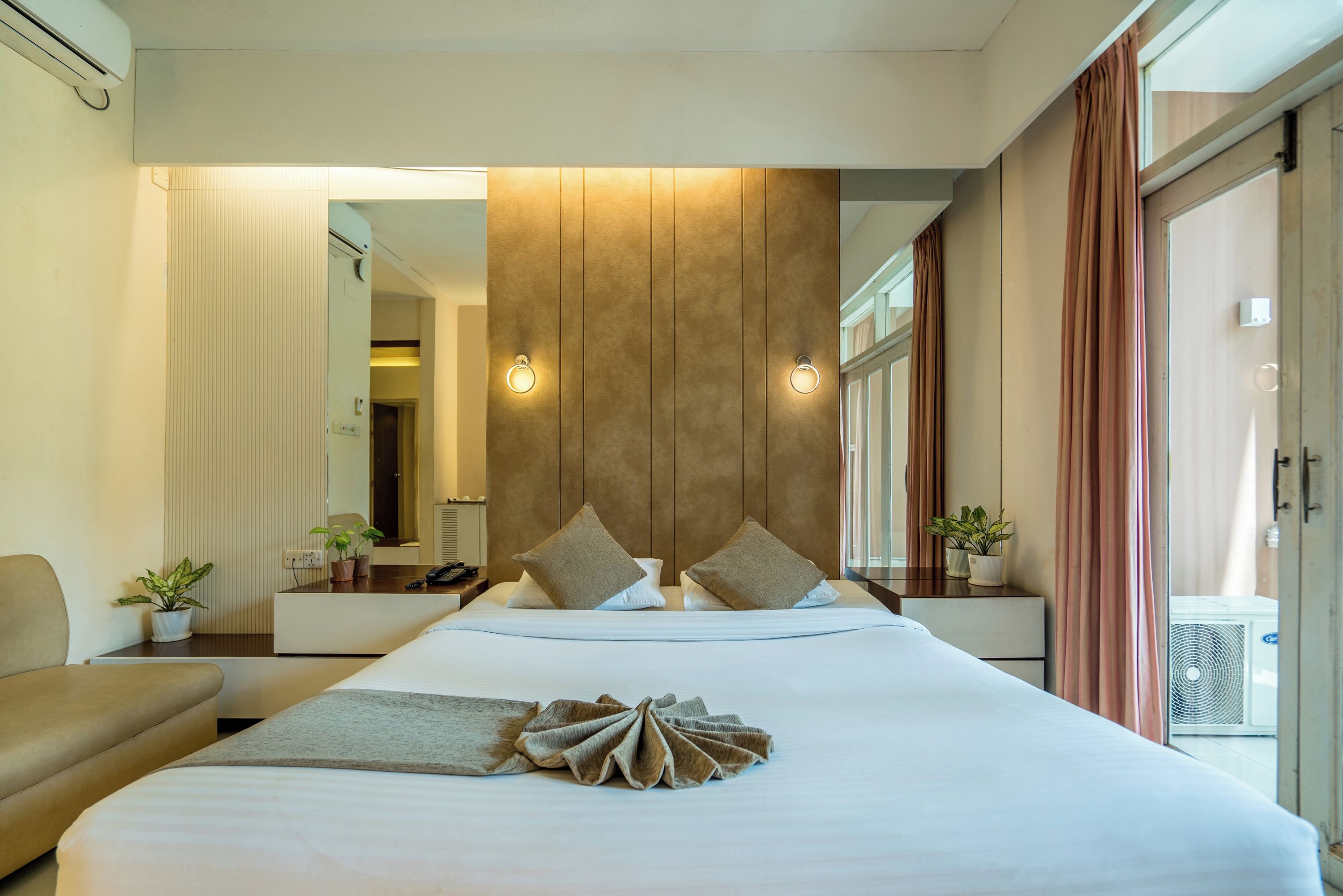 A hotel room with a large bed, bedside tables, a mirror, and a view of the outdoors.