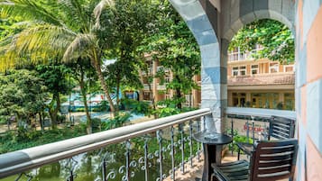 A balcony with a view of a pool and greenery, a table, and a chair.