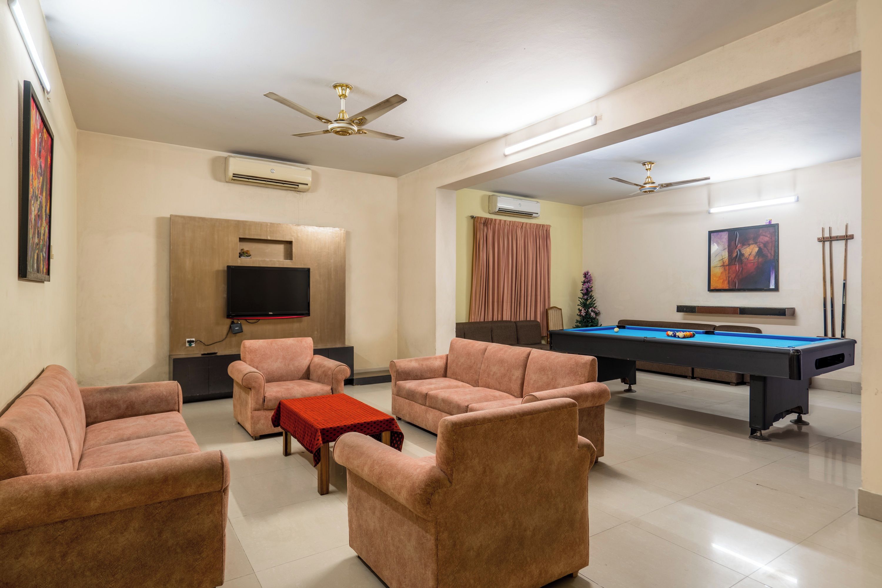 A modern living room with a pool table, sofas, a TV, and ceiling fans.