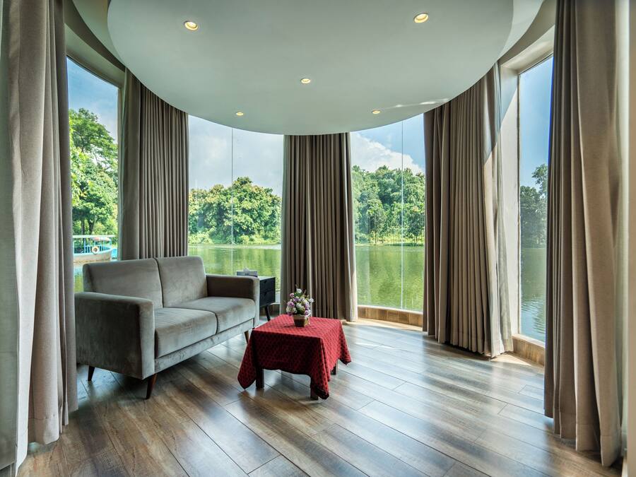 A room with a sofa, a small table with a red tablecloth, and a view of a lake through large windows.