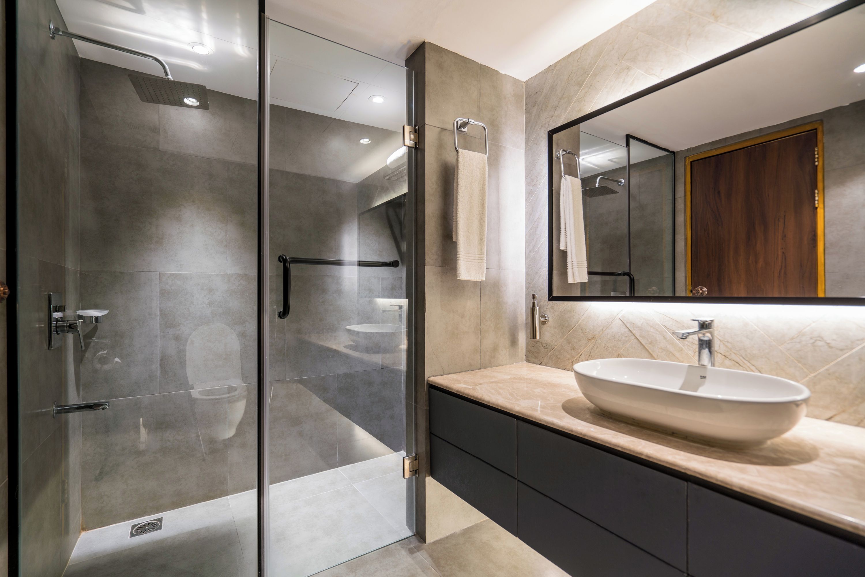 A modern bathroom with a glass-enclosed shower, a large mirror, and a beige vanity with a sink.