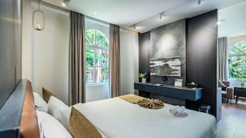A modern hotel room with a large bed, a desk, a chair, and a view of greenery outside.