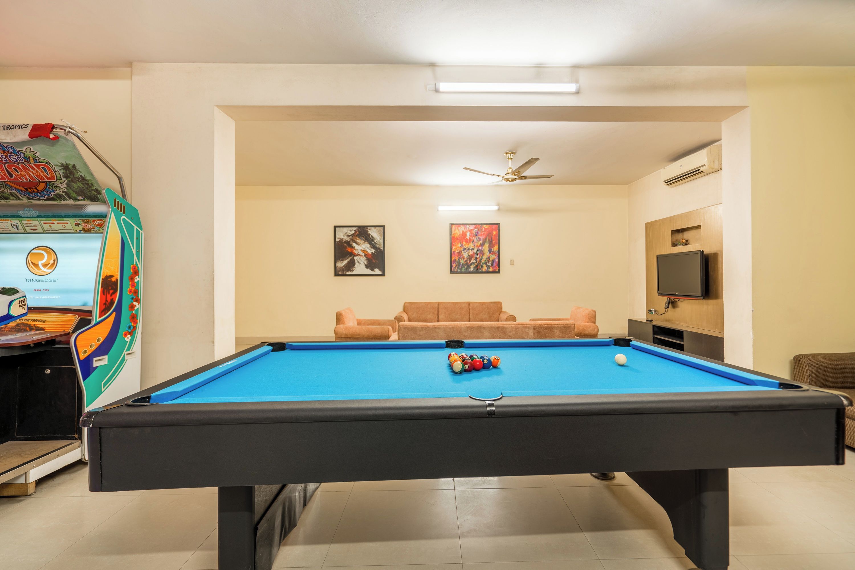 A pool table with a ceiling fan and two paintings on the wall.