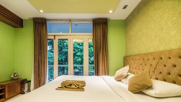 A hotel room with a large bed, a view of greenery through the window, and a wooden nightstand.