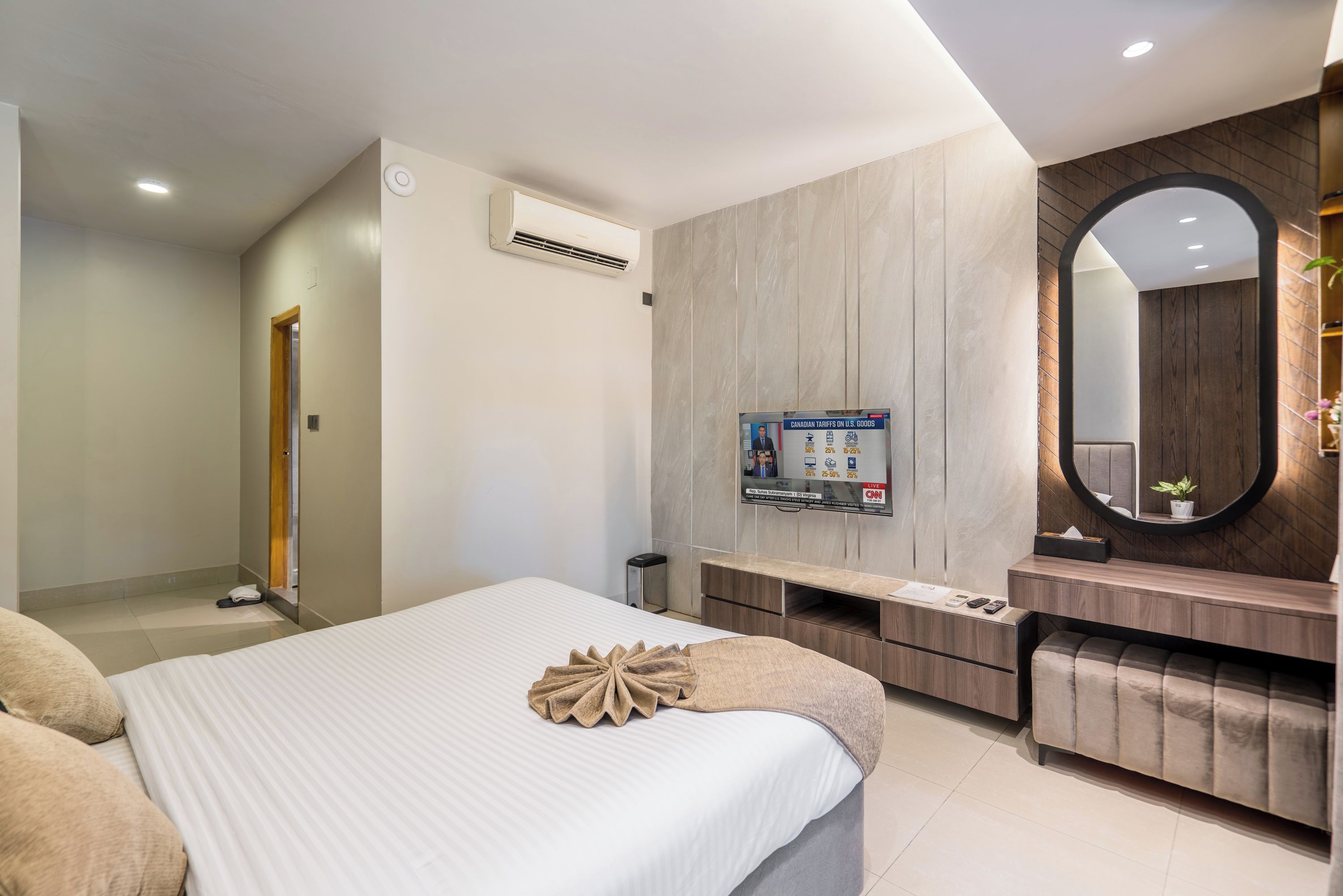 A modern bedroom with a bed, a TV mounted on the wall, a mirror, and a wooden vanity.