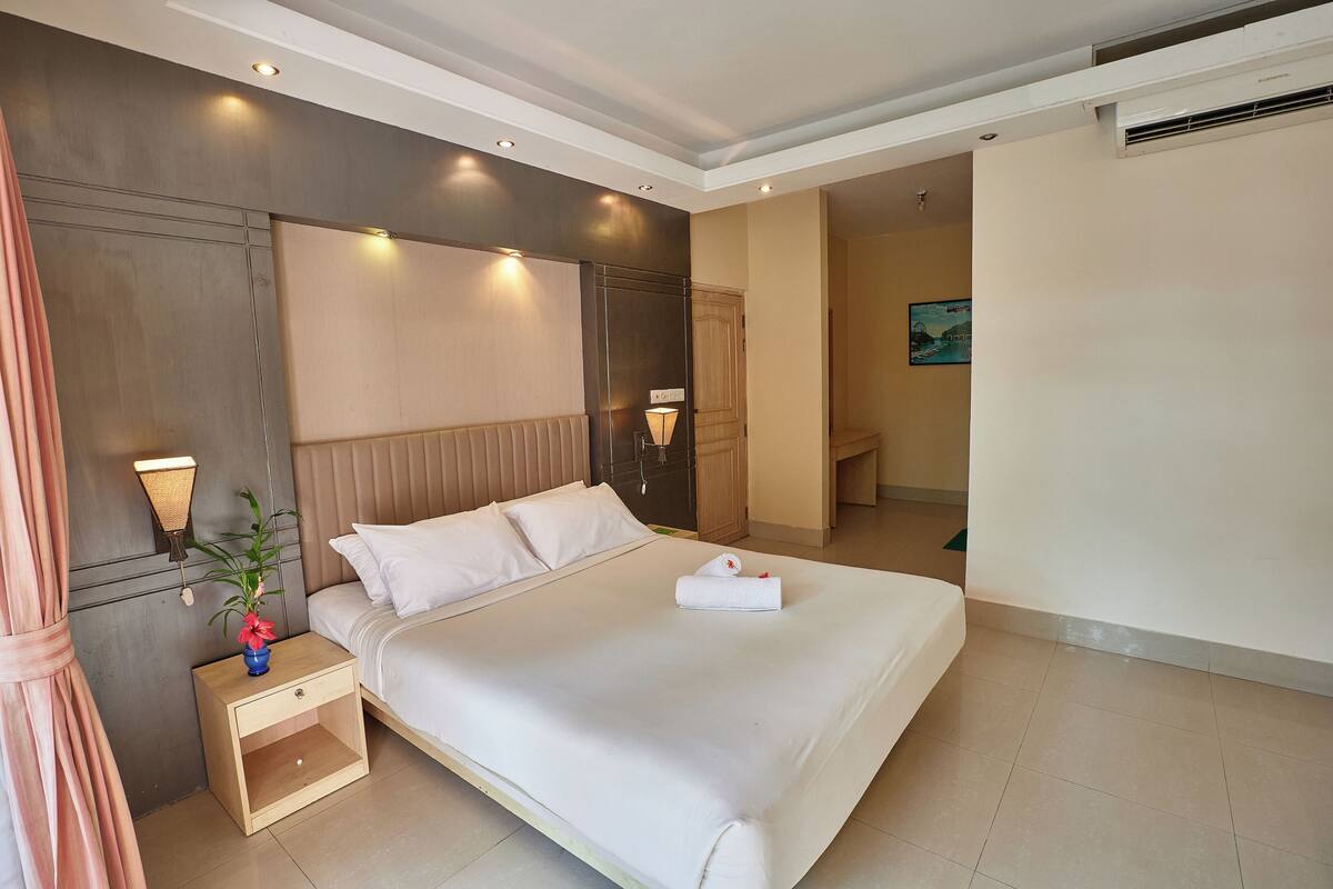 A modern hotel room with a large bed, bedside tables, a wall-mounted TV, and an air conditioning unit.