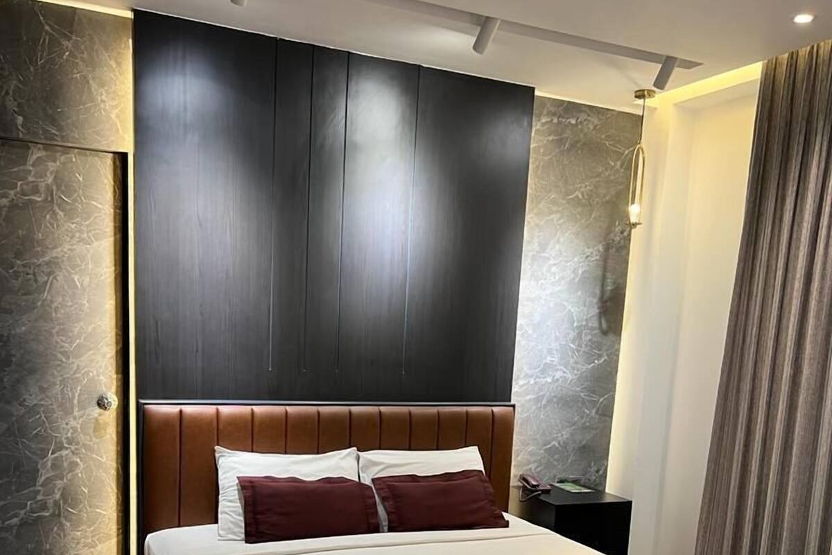 A modern hotel room with a large bed, dark wood headboard, and a marble-patterned nightstand.