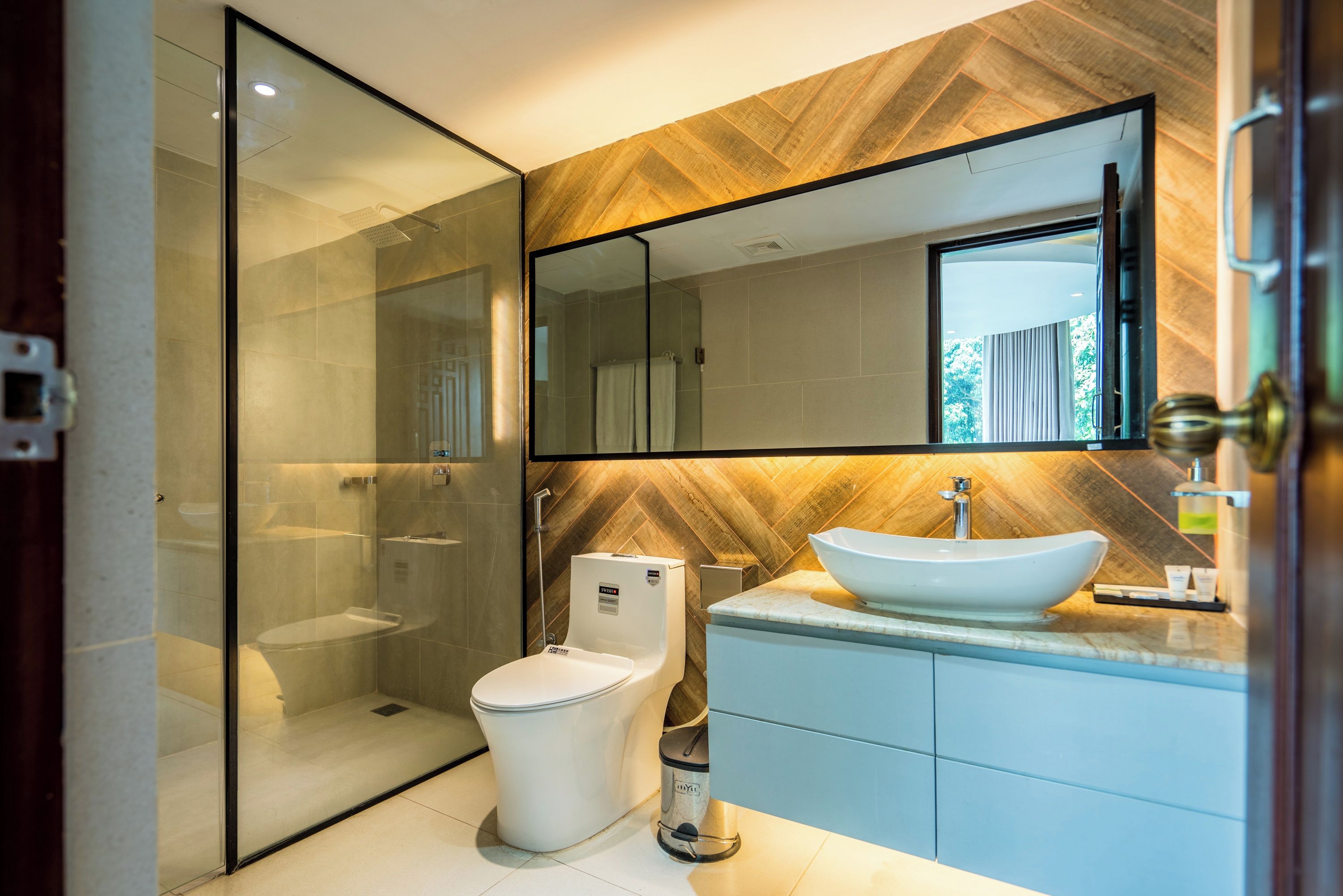 A modern bathroom with a glass shower enclosure, a toilet, a sink with a vessel basin, and a large mirror.