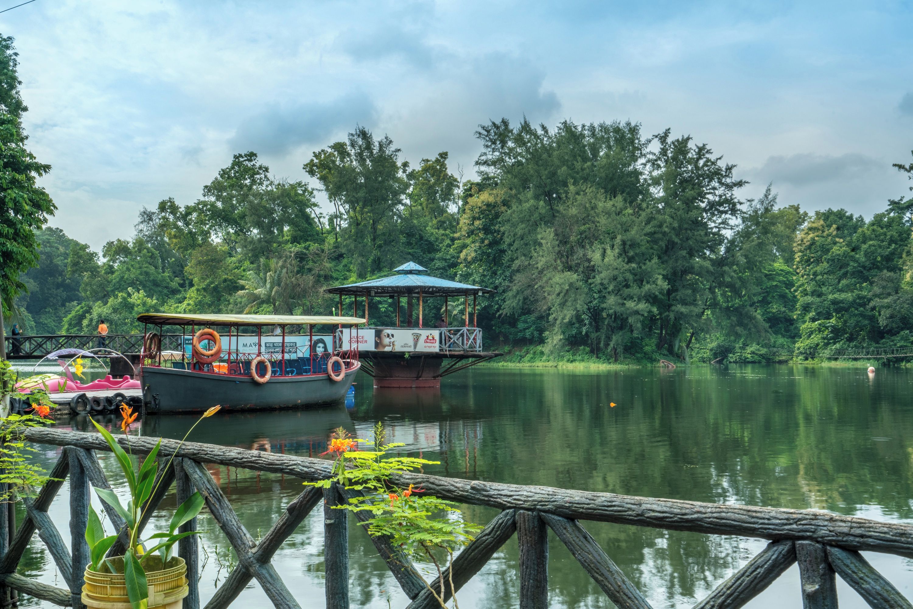 A calm lake with boats docked at a wooden pier, surrounded by dense greenery.