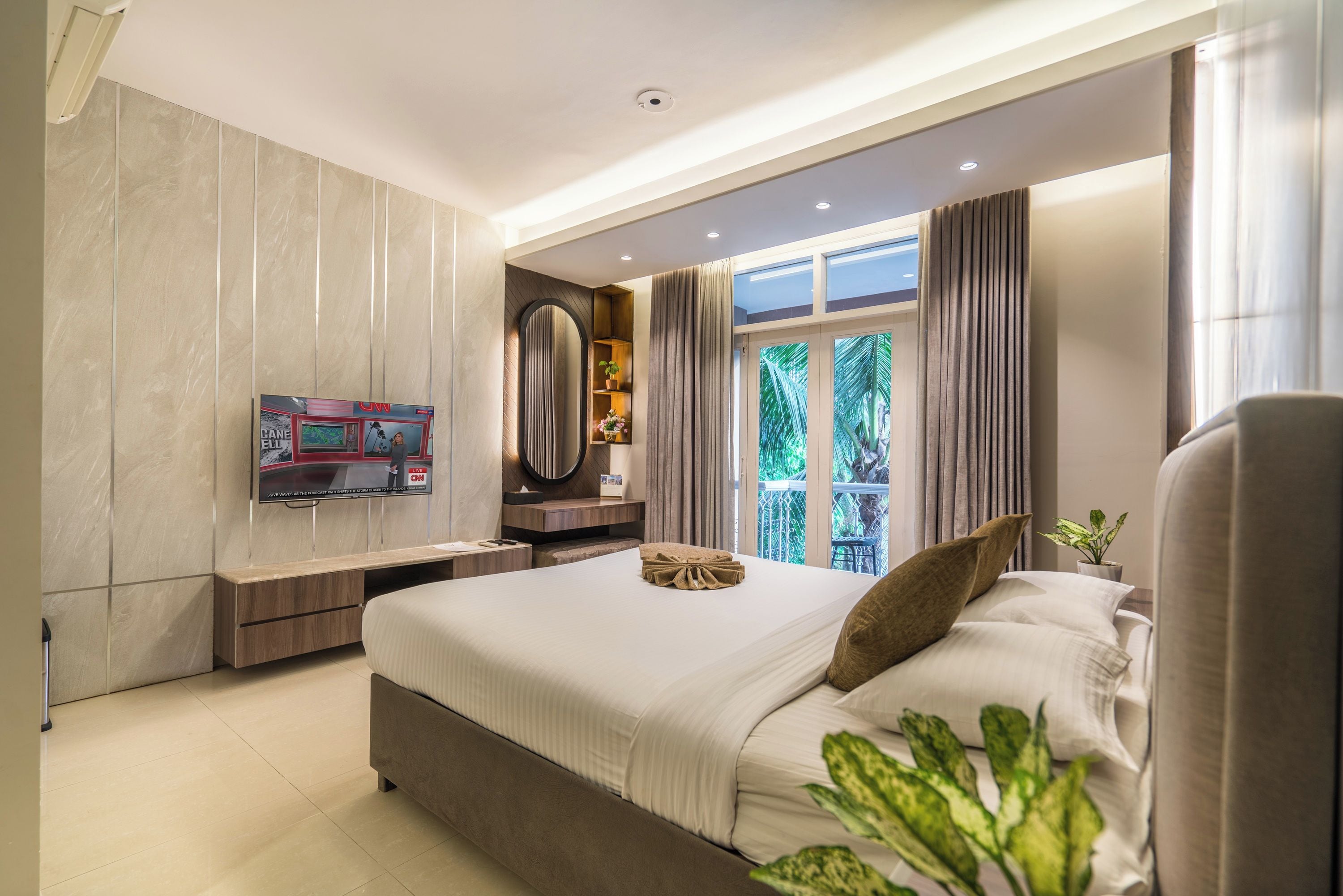 A modern hotel room with a large bed, a TV mounted on the wall, and a window with curtains.