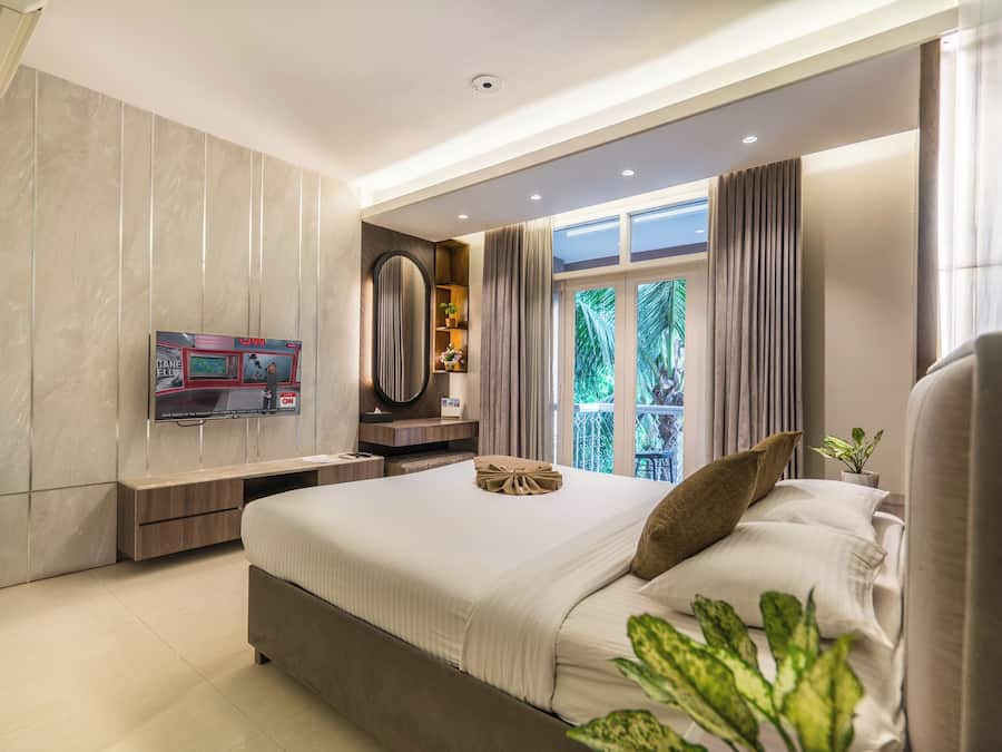 A modern hotel room with a large bed, a TV mounted on the wall, and a window with curtains.