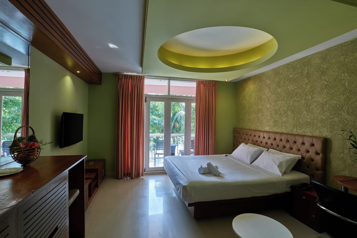 A hotel room with a large bed, a flat-screen TV, a wooden desk, and a view of the outdoors through a sliding door.
