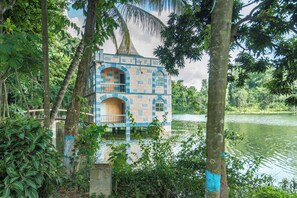 A house with a unique architectural style, surrounded by lush greenery and a body of water. - Foy's Lake Resort (Chittagong)