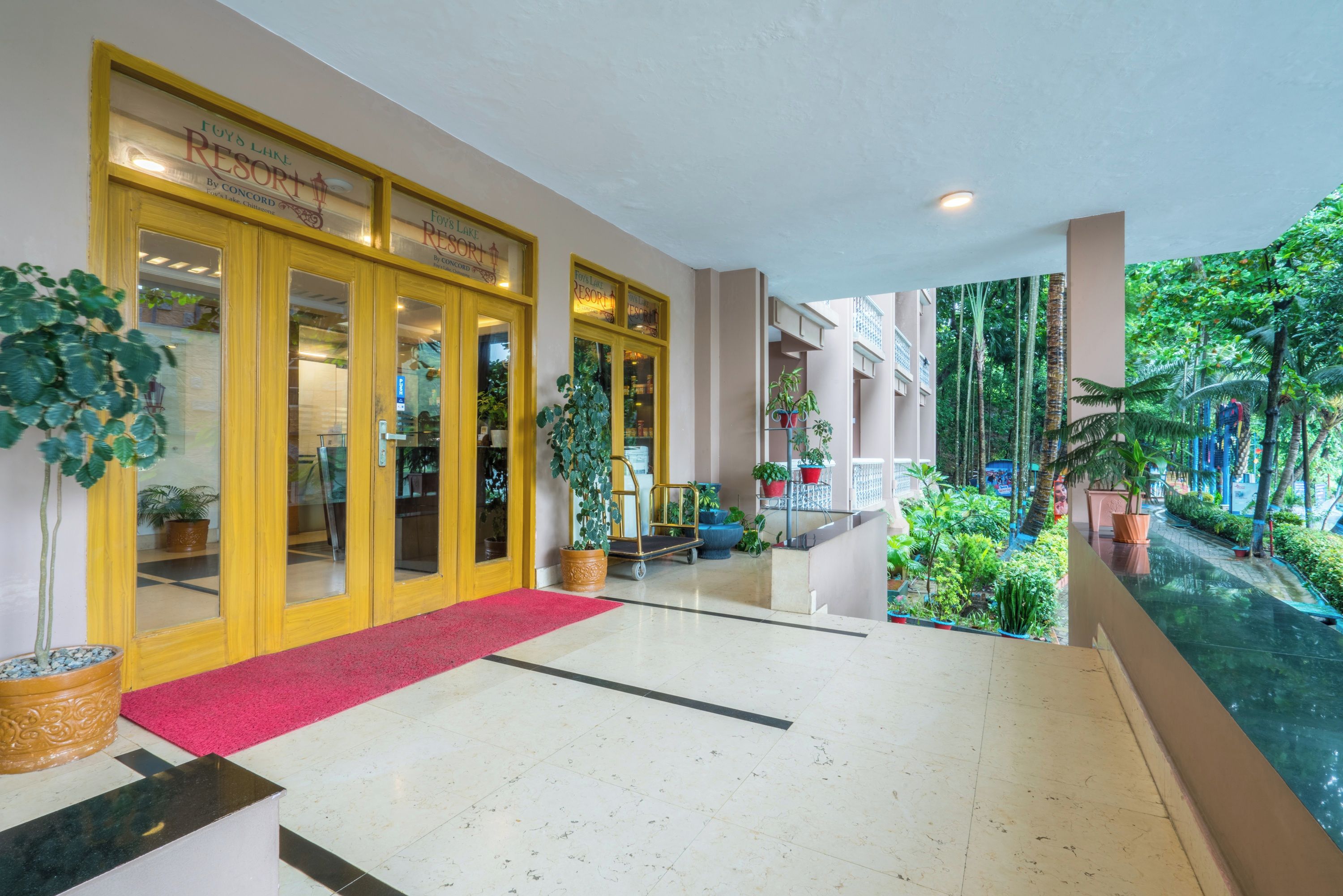 A hotel lobby with a red carpet, potted plants, and a view of a tropical garden.
