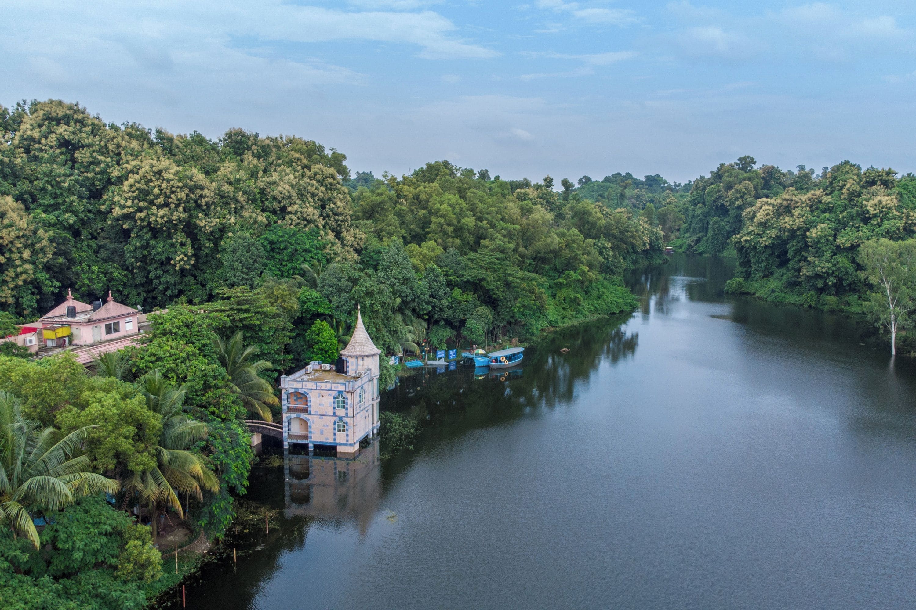 A river with boats, a small building with a tower, and dense greenery on both sides.