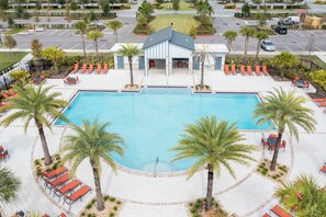 A swimming pool surrounded by palm trees and orange lounge chairs, with a building in the background. - Gorgeous 2Bd Apto Close to Disney Storey Lake 404 3191 (Kissimmee)