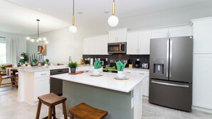 Una cocina moderna con armarios blancos, electrodomésticos de acero inoxidable y una isla central con taburetes.