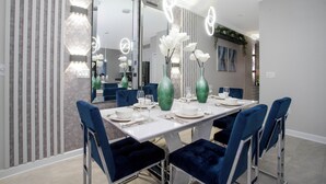 Een moderne eetruimte met een witte tafel voor vier personen, blauwe gestoffeerde stoelen en decoratieve vazen met witte bloemen.