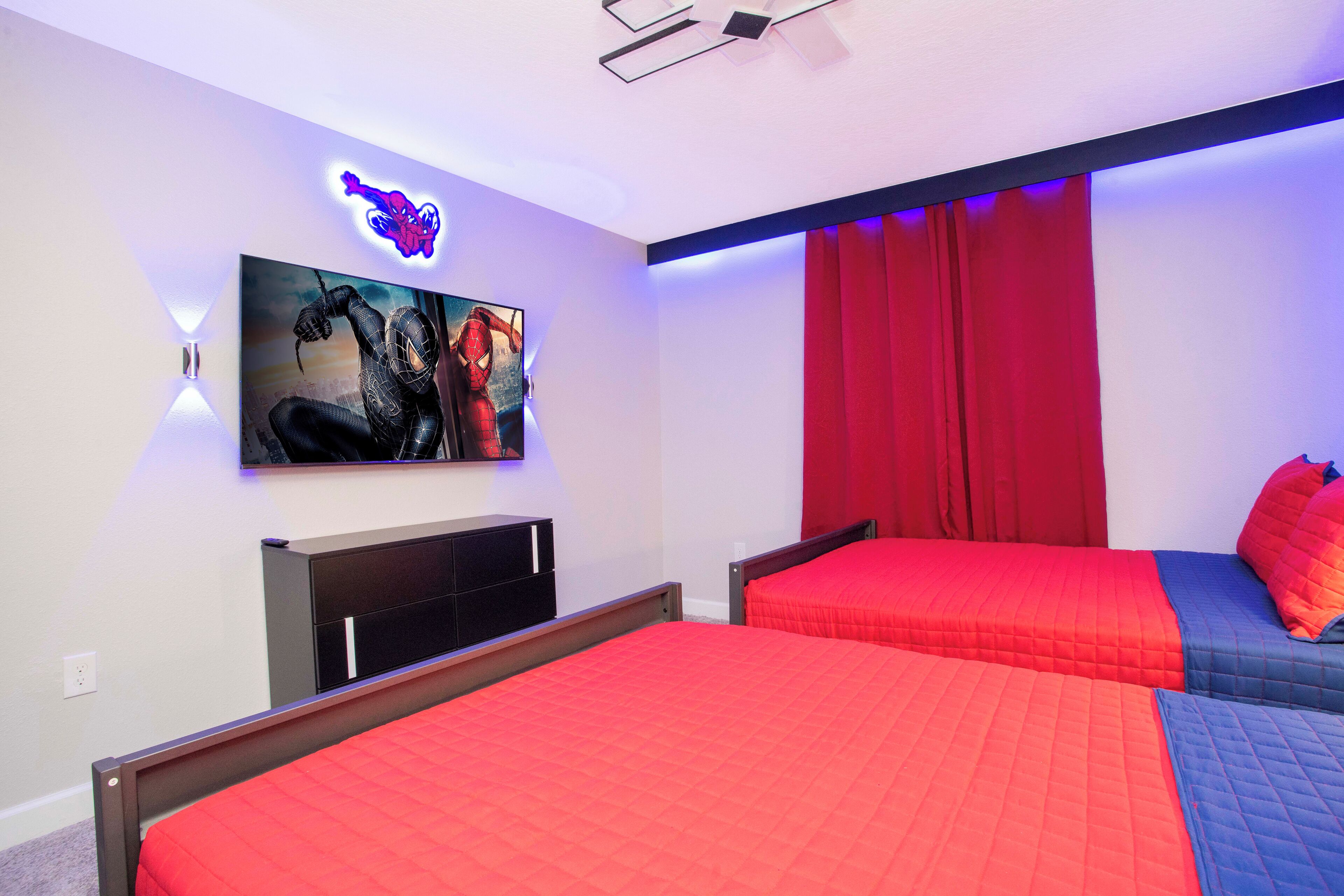 A bedroom with two beds, a wall-mounted TV, and red curtains.