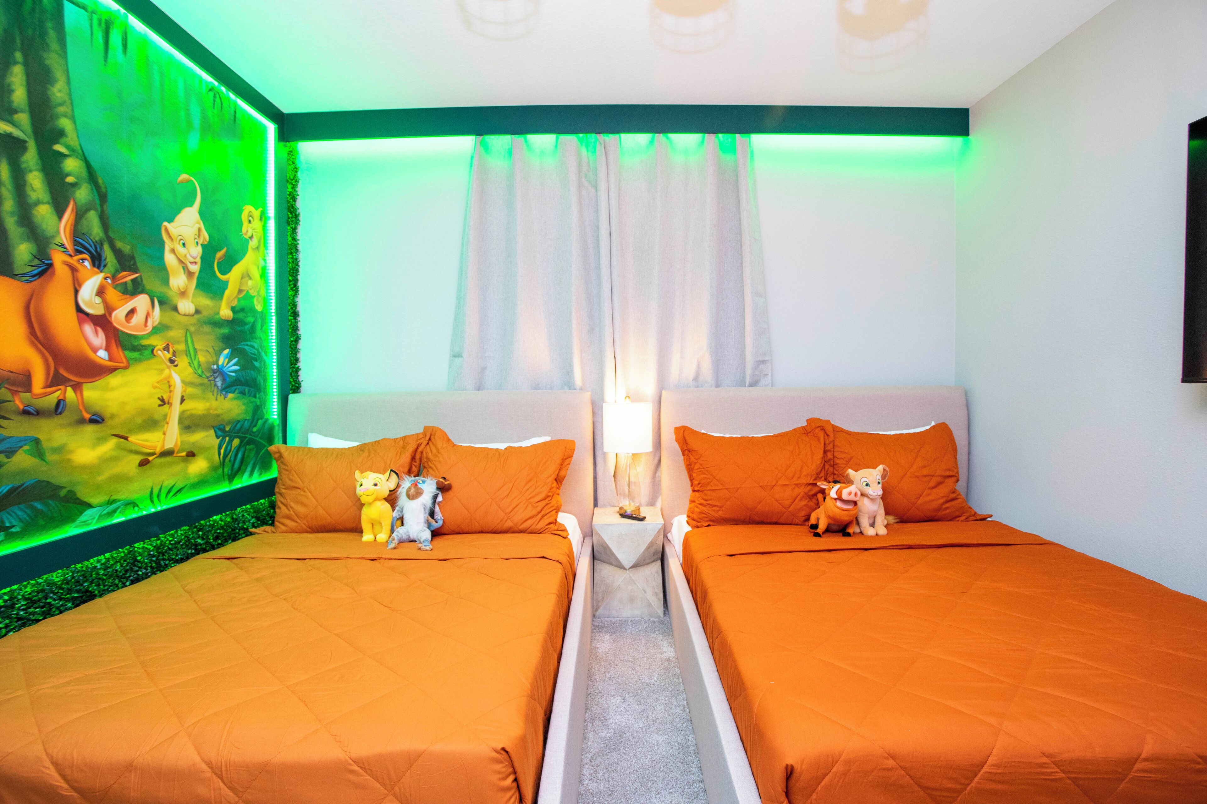 Habitación de hotel con dos camas, ropa de cama naranja, un mural de personajes animados en la pared y una ventana con cortinas.