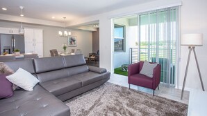 A modern living room with a grey sofa, a purple armchair, and a large window with a view of greenery.