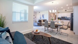 A modern kitchen with white cabinets, a dining area with a table and chairs, and a living room with a sofa and a coffee table.