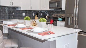 A modern kitchen with white cabinets, a stainless steel refrigerator, a microwave, and a built-in oven.