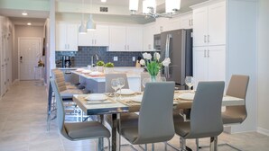 A modern kitchen with white cabinets, a central island, and a dining area with chairs and a table set for six.
