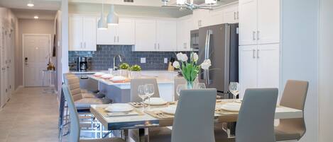 A modern kitchen with white cabinets, a central island, and a dining area with chairs and a table set for six.