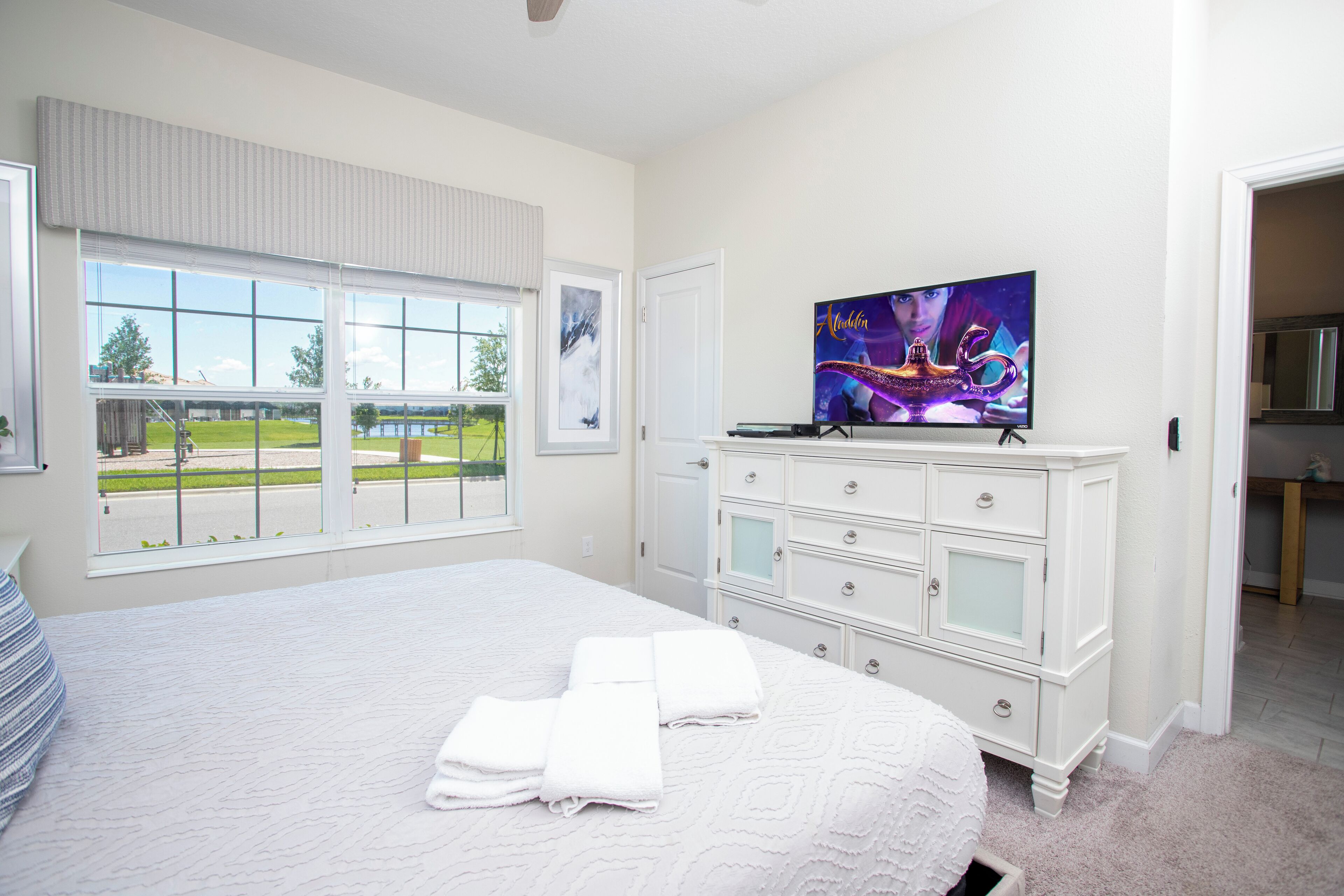 Une chambre à coucher avec un grand lit, une commode, un téléviseur et une fenêtre donnant sur un parc.