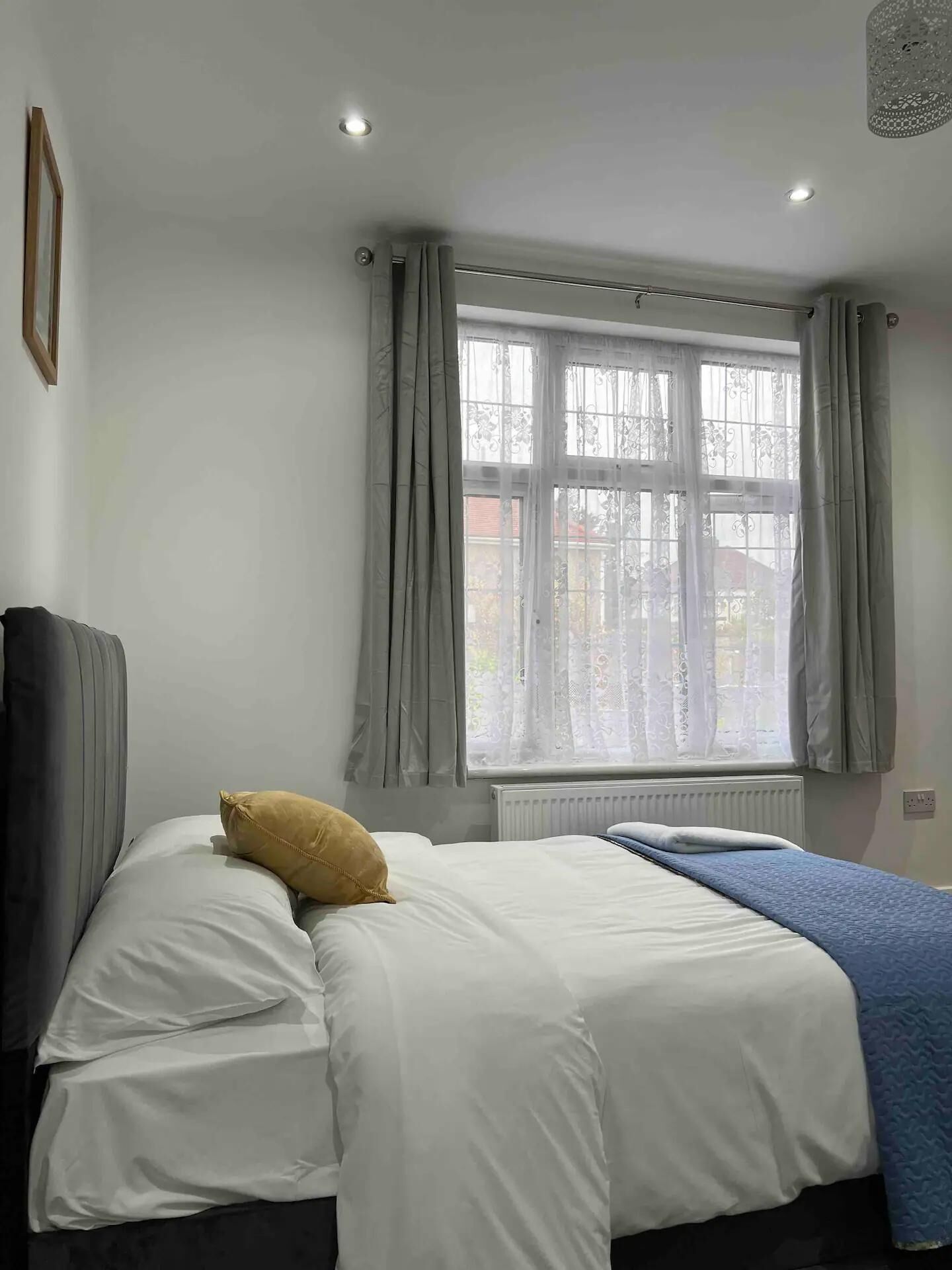 Een slaapkamer met een bed, een radiator, een raam met gordijnen en een plafondlamp.
