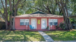 A single-story house with a red exterior, a front porch with a blue chair, and a mailbox.