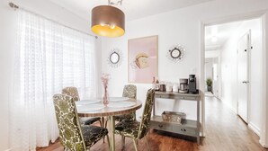 A dining area with a round table, patterned chairs, a hanging light fixture, decorative mirrors, and a coffee station.