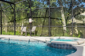 Une piscine extérieure avec un jacuzzi, entourée d’une clôture en métal et d’arbres.