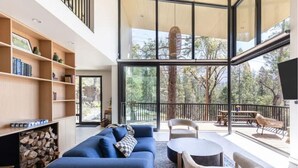 A modern living room with a blue sofa, a coffee table, and a bookshelf. There is a balcony with outdoor furniture. - Modern Sophistication Bathed in Natural Light (Wawona)