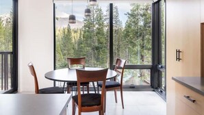 A dining area with a round table and chairs, large windows with a view of trees and mountains, and pendant lights. - Modern Sophistication Bathed in Natural Light (Wawona)