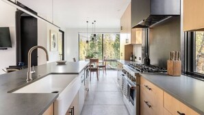 A modern kitchen with a central island, stainless steel appliances, and a large window offering a view of trees. - Modern Sophistication Bathed in Natural Light (Wawona)