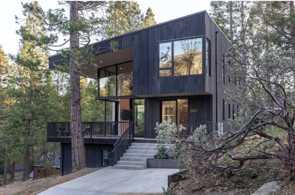 A modern two-story house with a balcony, surrounded by trees.