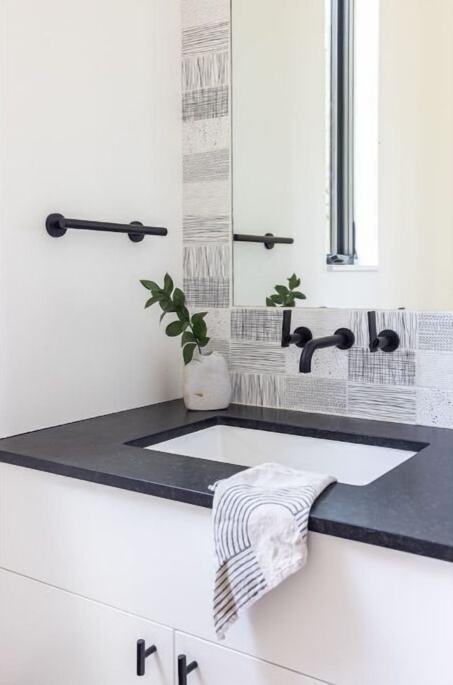 A bathroom with a black countertop, white cabinets, a large mirror, and a towel hanging on the wall.