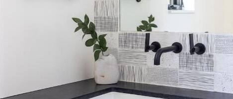 A bathroom with a black countertop, white cabinets, a large mirror, and a towel hanging on the wall.