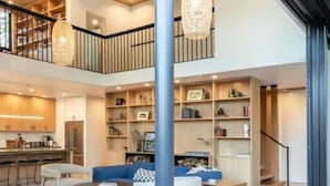 A spacious living area with a high ceiling, a staircase, and a kitchen area. - Modern Sophistication Bathed in Natural Light (Wawona)