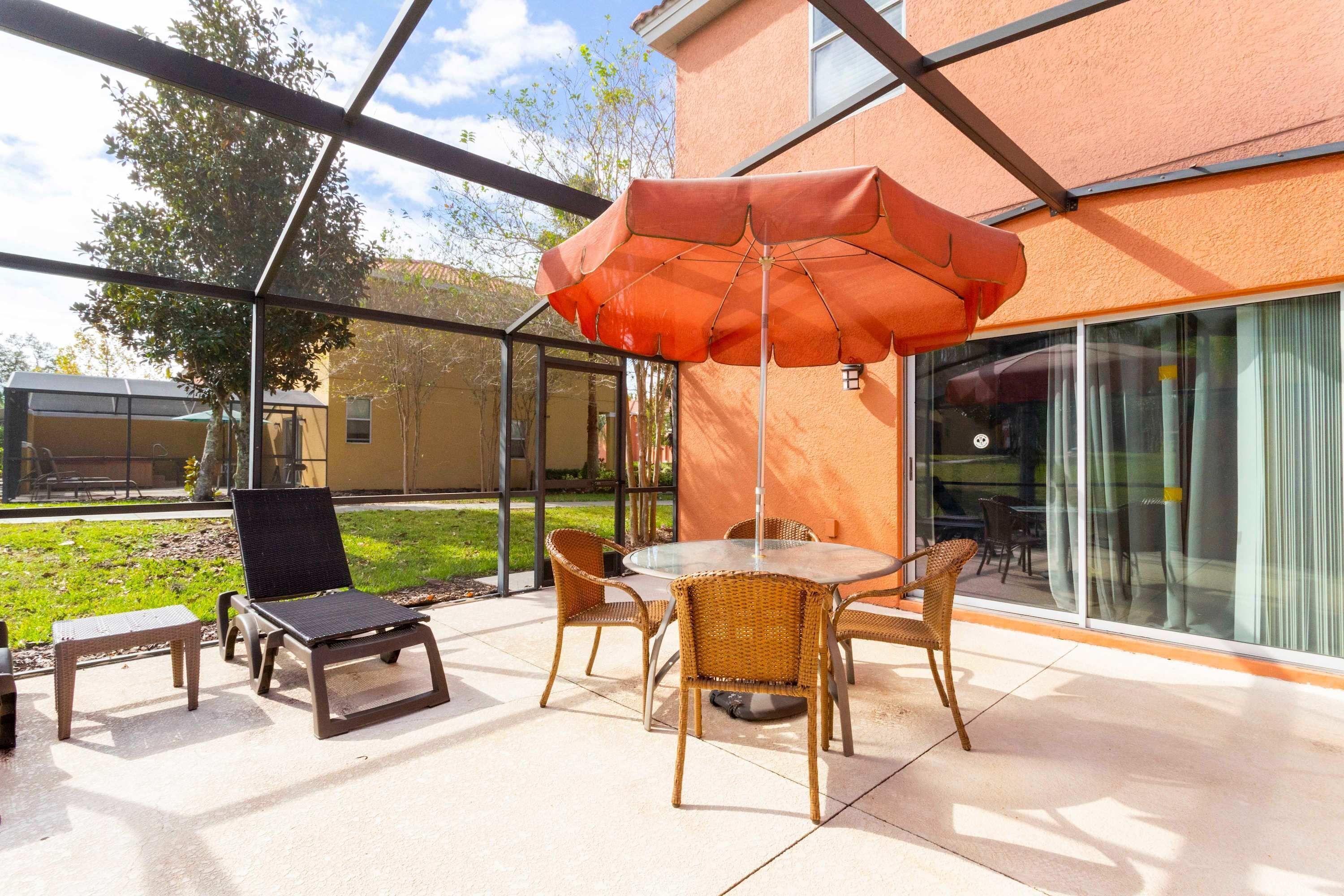 Une terrasse extérieure aménagée avec des meubles en osier, une table en verre et un grand parasol.