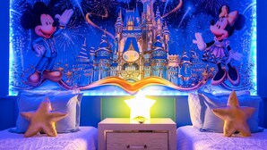 Ein Schlafzimmer mit Wandmalerei zum Thema Disney, zwei Betten, einem Nachttisch und sternförmigen Kissen.