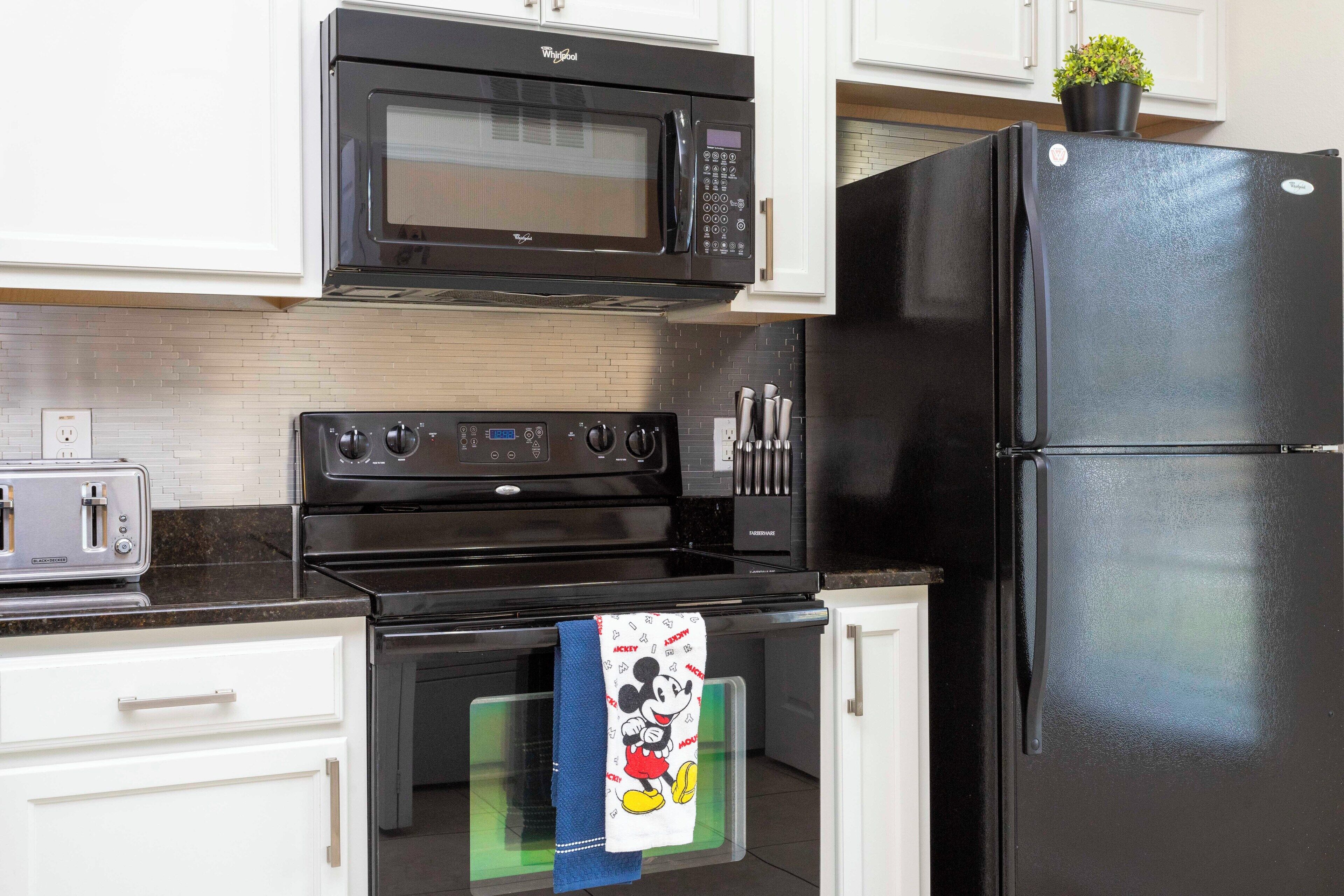 A kitchen with a black microwave, stove, and refrigerator, a toaster, and a Mickey Mouse towel hanging on the oven door.