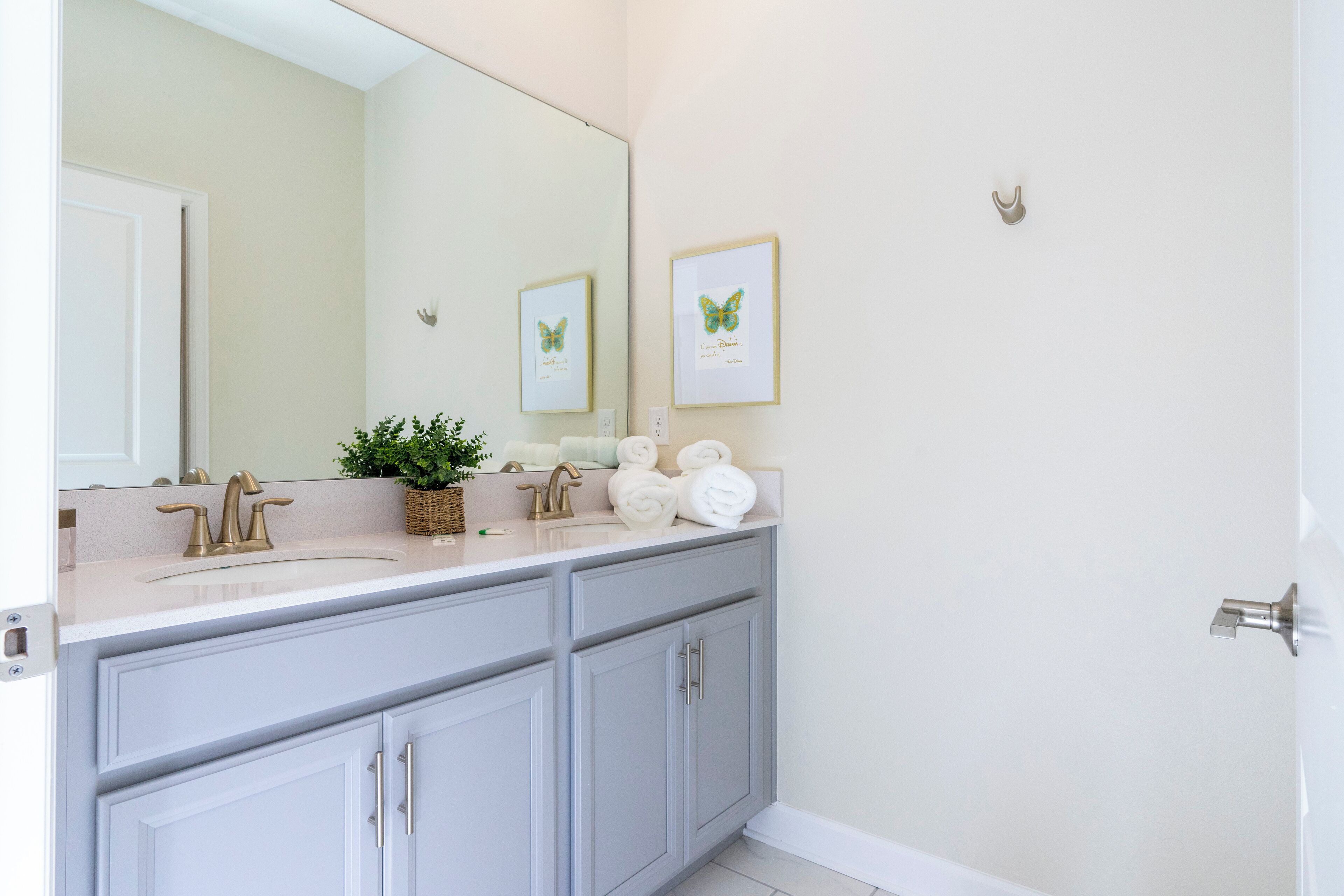 A bathroom with a double sink, a large mirror, and framed artwork on the wall.
