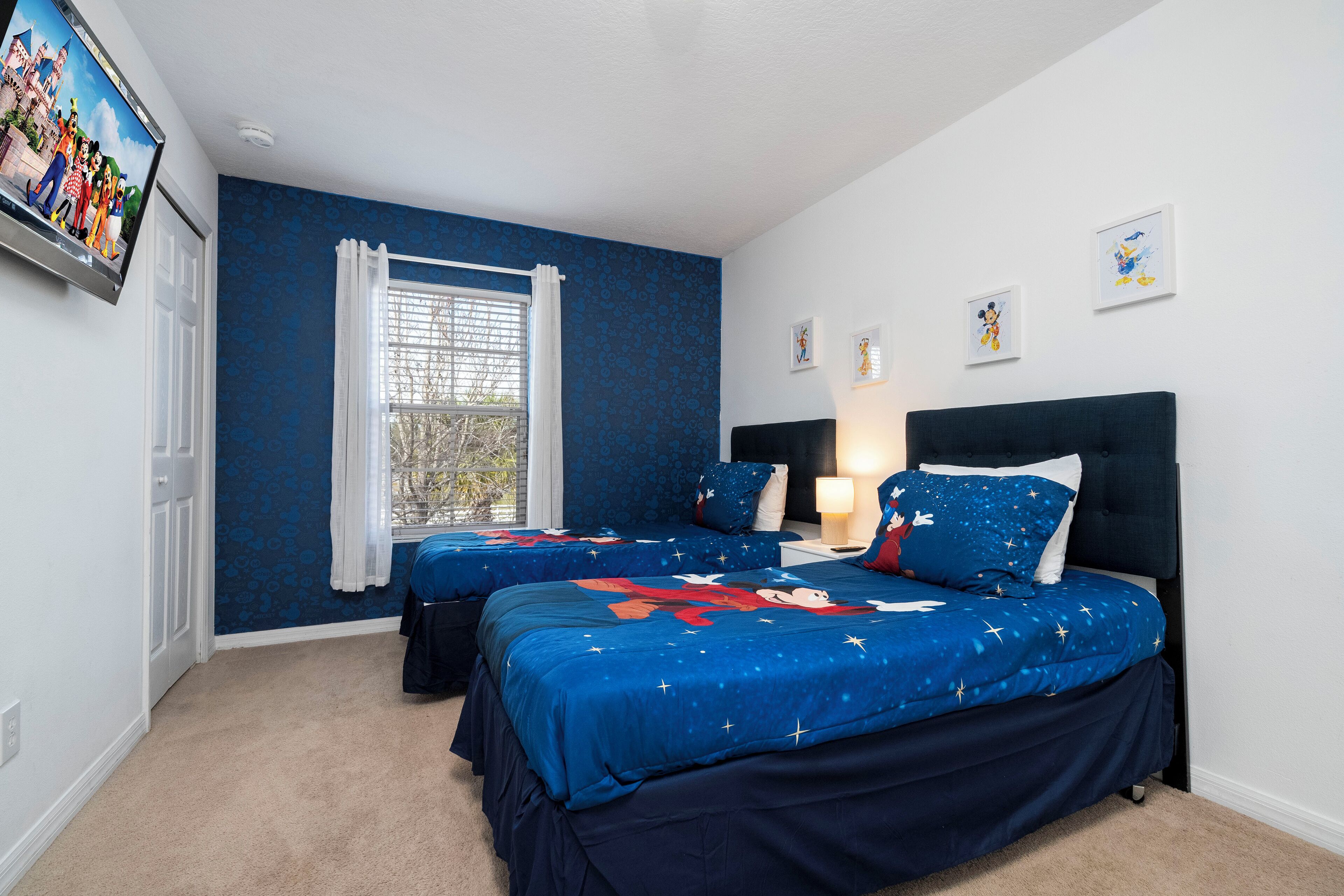 A bedroom with two beds, a window with curtains, and wall art.