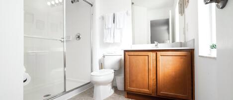 Un baño moderno con cabina de ducha de vidrio, inodoro blanco y muebles de madera.